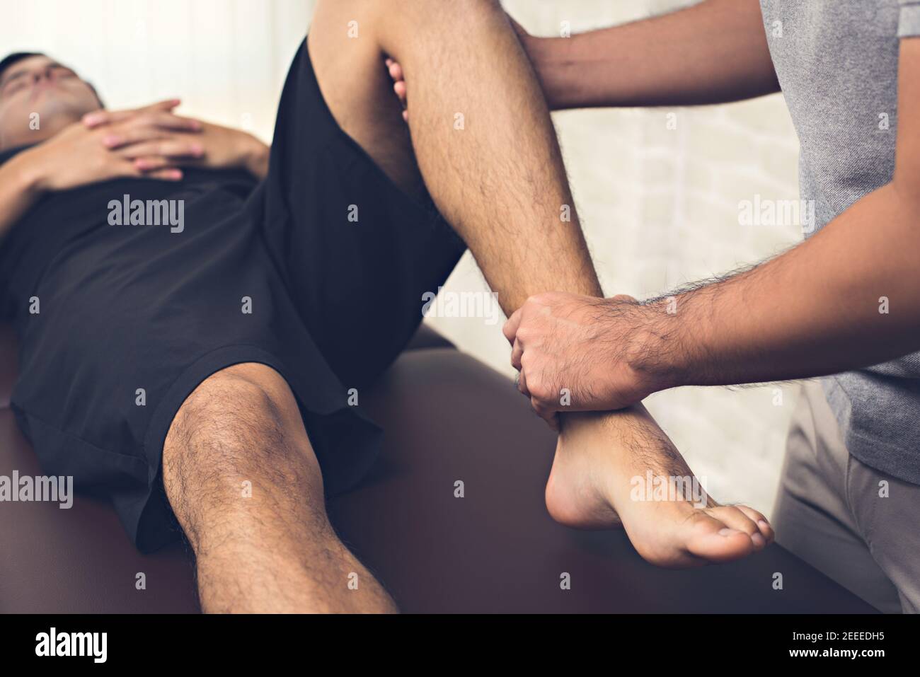 Terapista che cura la gamba ferita del paziente maschile dell'atleta in clinica - concetto di fisioterapia sportiva Foto Stock