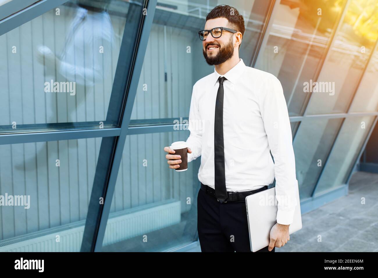 Uomo d'affari riuscito con il laptop che tiene una tazza di caldo bevi in mano sul suo modo di lavorare in città via Foto Stock