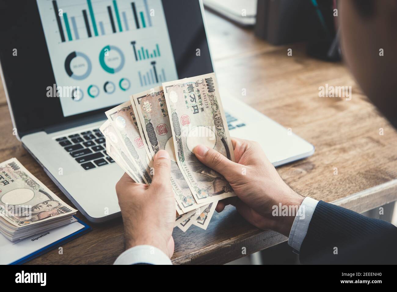 Uomo d'affari che conta denaro, banconote giapponesi yen, di fronte al computer portatile al banco di lavoro - concetto finanziario e di investimento Foto Stock