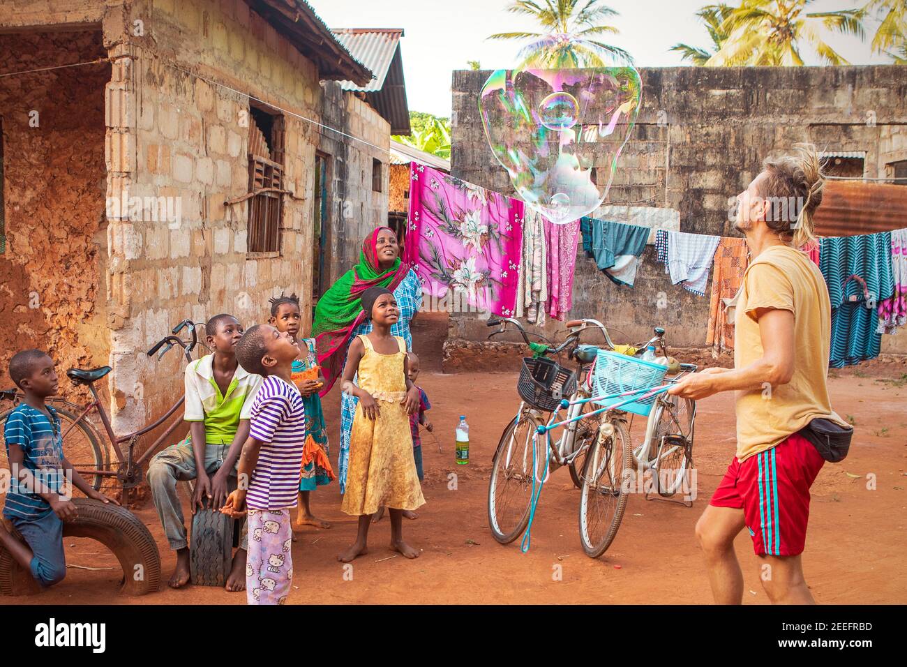 Makunduchi, Zanzibar, Tanzania - 01.16.2021: Etnia caucasica, uomo europeo che gioca con bambini di etnia nera. Volontariato di beneficenza Foto Stock