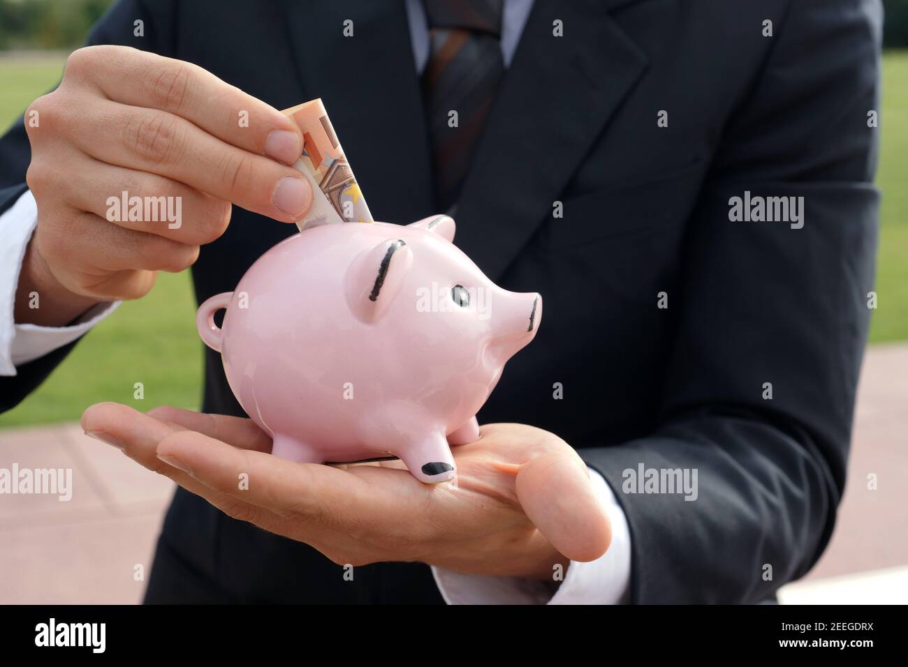 L'uomo d'affari alimenta la banca dei piggy con la banconota tedesca - risparmio di concetto fondi di prestito che investono denaro Foto Stock