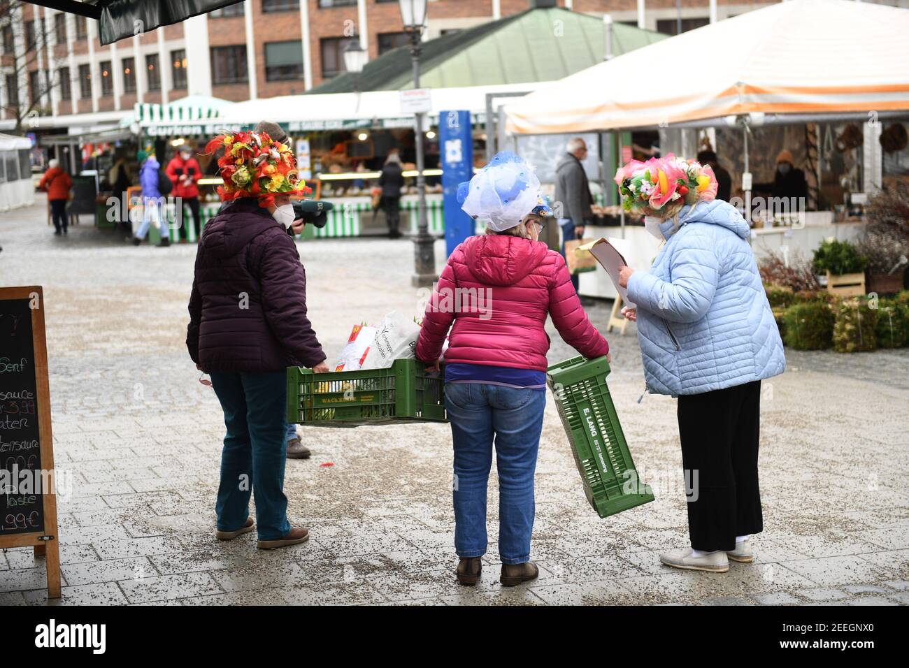 Monaco, Germania. 16 Feb 2021. Le donne del mercato camminano attraverso il Viktualienmarkt con le casse di frutta il martedì di Shrove. La danza tradizionale delle donne di mercato non si svolge quest'anno a causa della pandemia di Corona. Credit: Felix Hörhager/dpa/Alamy Live News Foto Stock