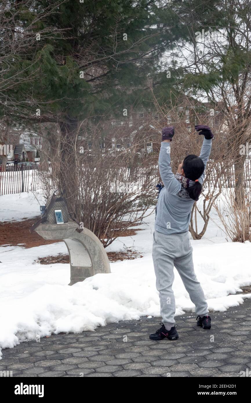 In una fredda mattinata invernale, una donna cinese americana balla ed esercizi di musica dal suo iphone. A Flushing, Queens, New York City. Foto Stock