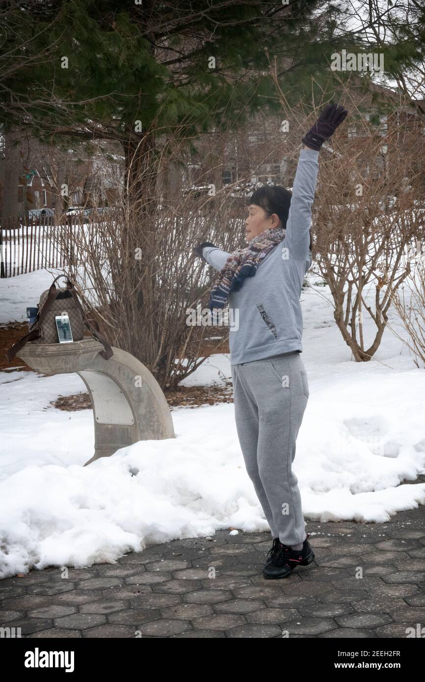 In una fredda mattinata invernale, una donna cinese americana balla ed esercizi di musica dal suo iphone. A Flushing, Queens, New York City. Foto Stock