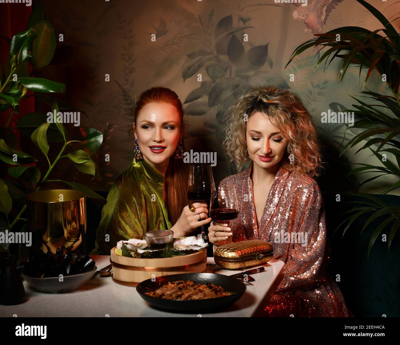Due ricche e meravigliose donne amiche in abiti alla moda hanno tempo nel ristorante di pesce mangiare ostriche, bere vino Foto Stock