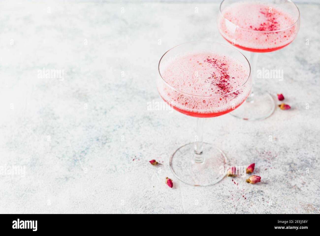 Cocktail alcolico rosa con limonata, champagne o Martini in un bicchiere di champagne, con schiuma e decorato con boccioli di rosa, cocktail come Daiquiri, Foto Stock