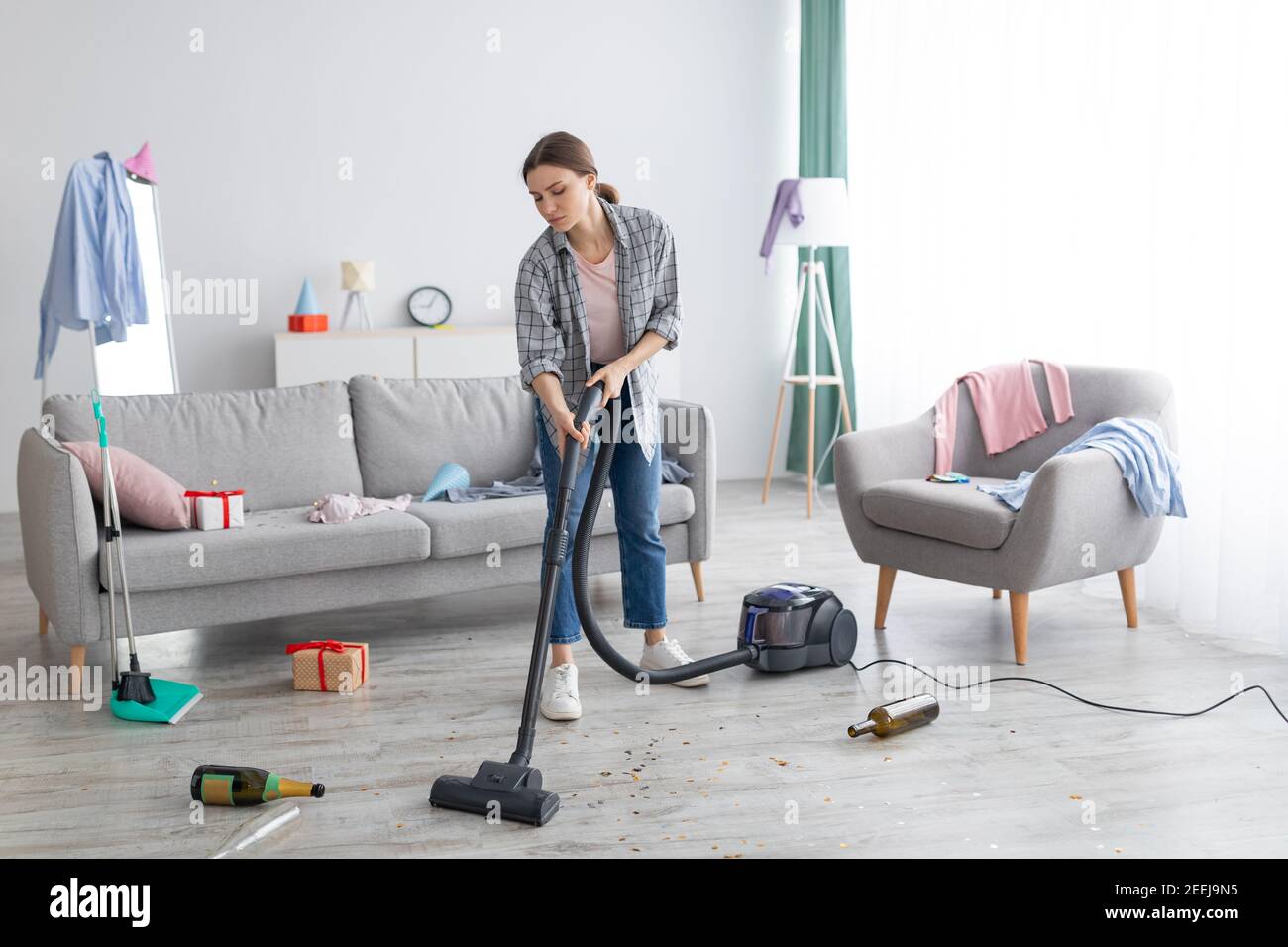 Infelice giovane donna che vacuuming appartamento disordinato dopo la festa, ripulendo il caos dopo la celebrazione di festa, spazio di copia Foto Stock