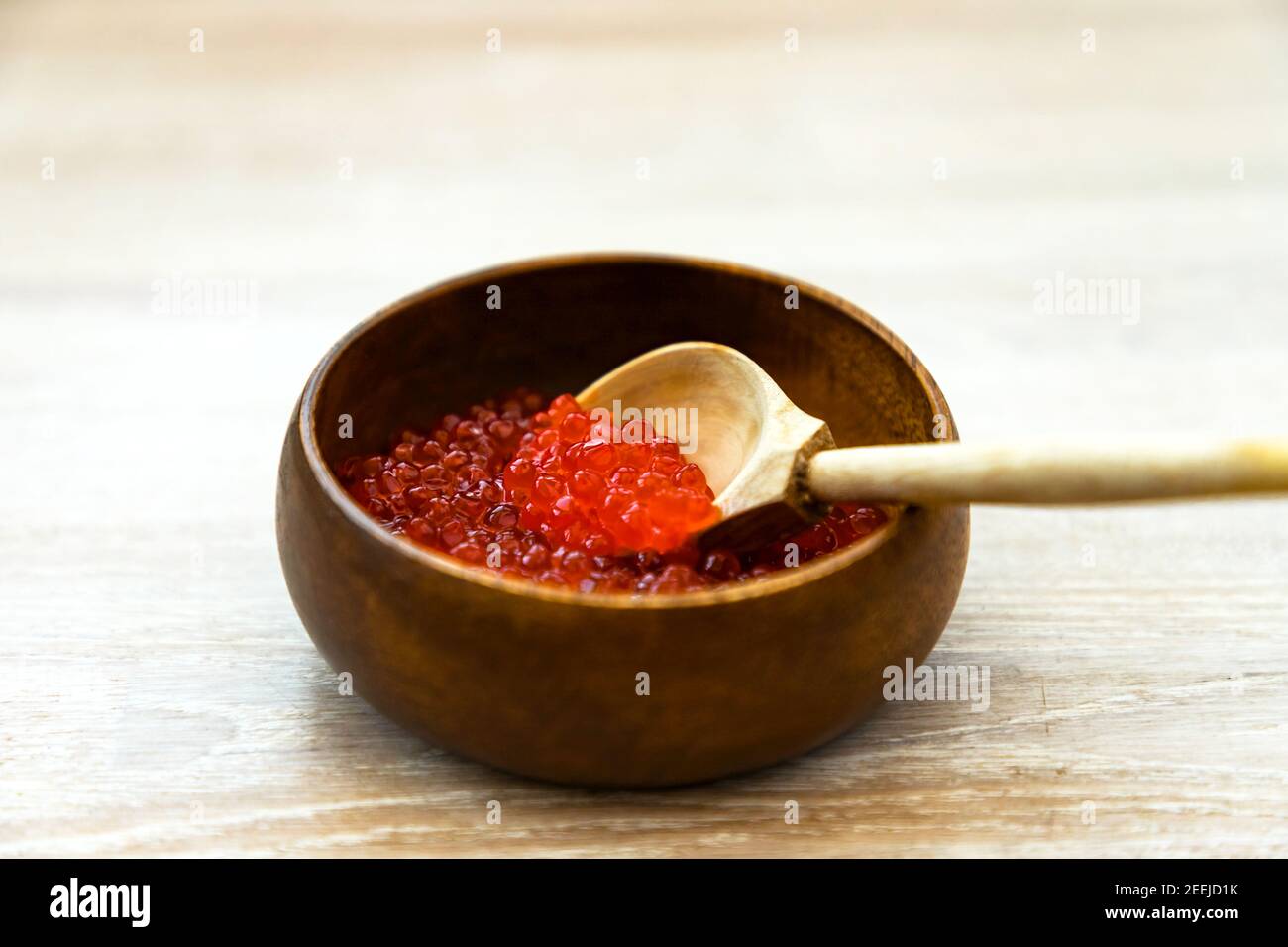 Caviale rosso fresco in ciotola di bambù con cucchiaio di legno rustico in legno bianco sbiancato sfondo tavolo Foto Stock