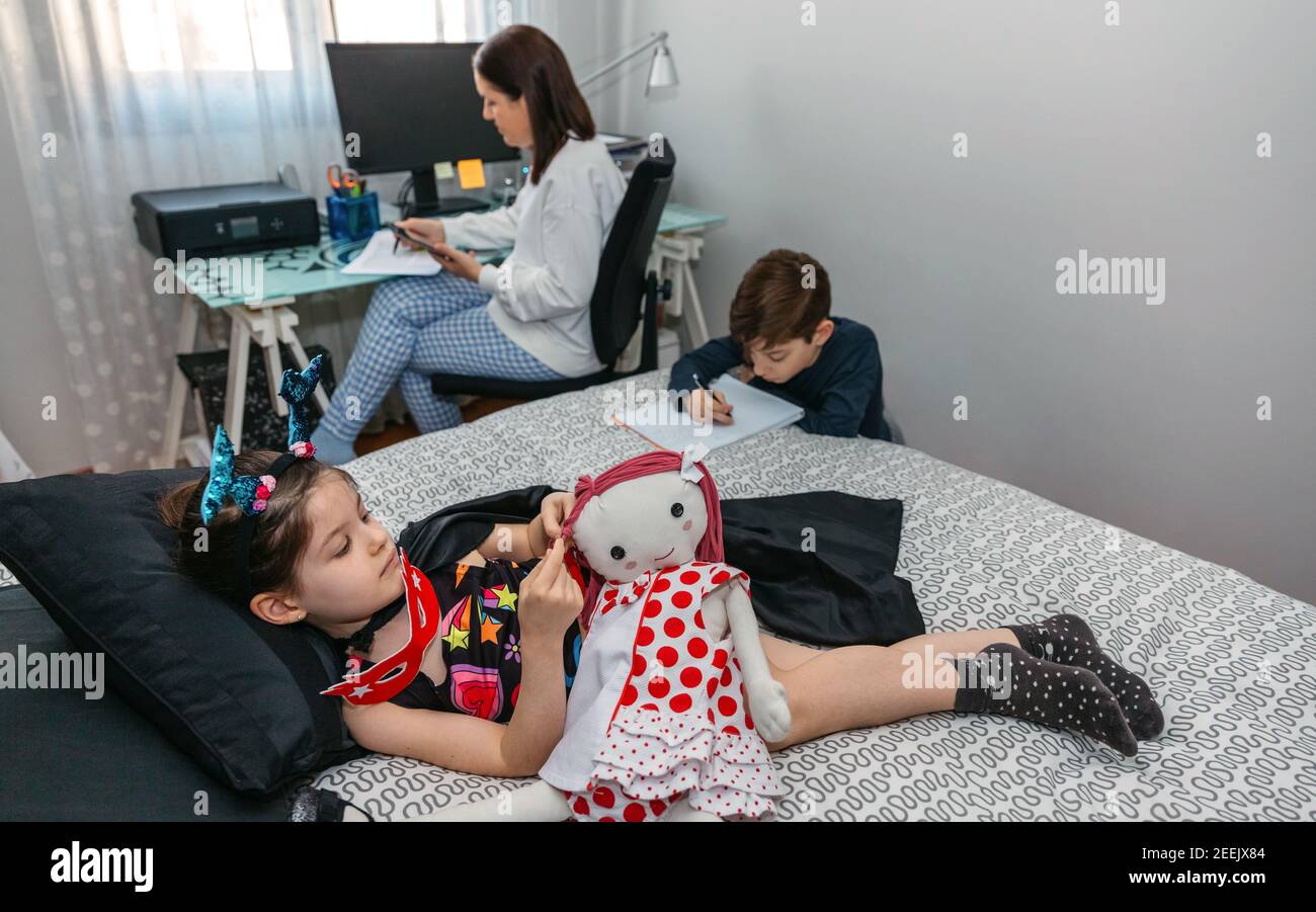 I bambini giocano e fanno i compiti mentre la loro madre lavora a casa. Conciliazione concetto di lavoro familiare Foto Stock