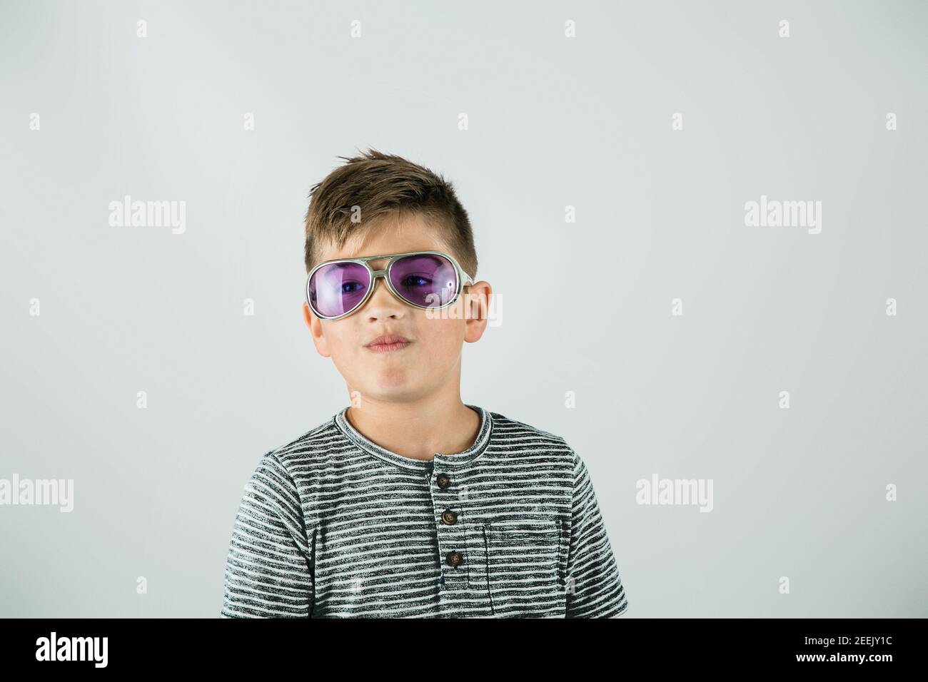 Piccolo ragazzo caucasico in piedi in un ambiente studio su uno sfondo bianco con occhiali da sole viola stella rock e atteggiamento. Foto Stock