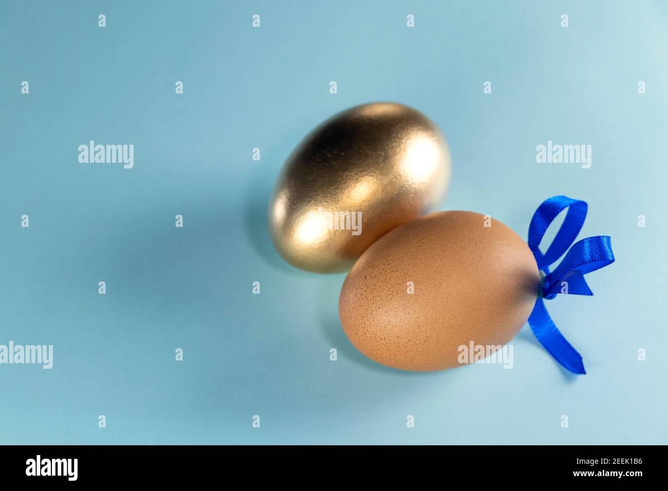 Far rosolare l'uovo con il nastro blu e l'uovo dorato. Buon concetto di Pasqua. Due uova con nastro su sfondo blu pastello con spazio per la copia. Foto Stock