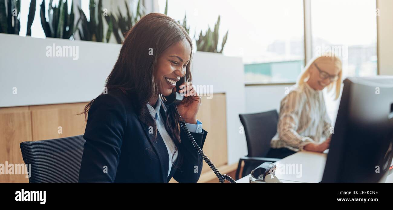 Ridendo giovane americano africano imprenditrice parlando al telefono mentre si lavora con un collega presso un Ufficio escursioni Foto Stock