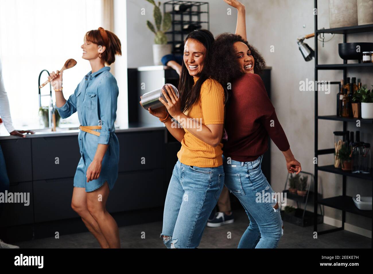 Gruppo vario di giovani donne ridenti che ballano e cantano durante una cena in cucina di un amico Foto Stock