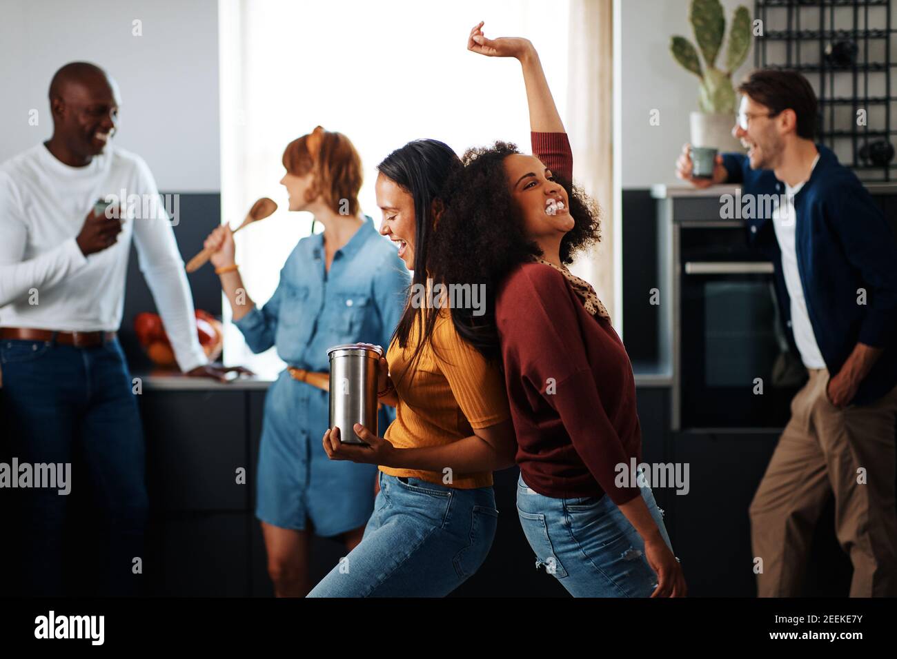 Gruppo ridente di amici diversi che cantano e ballano insieme durante una festa in cucina di un amico Foto Stock
