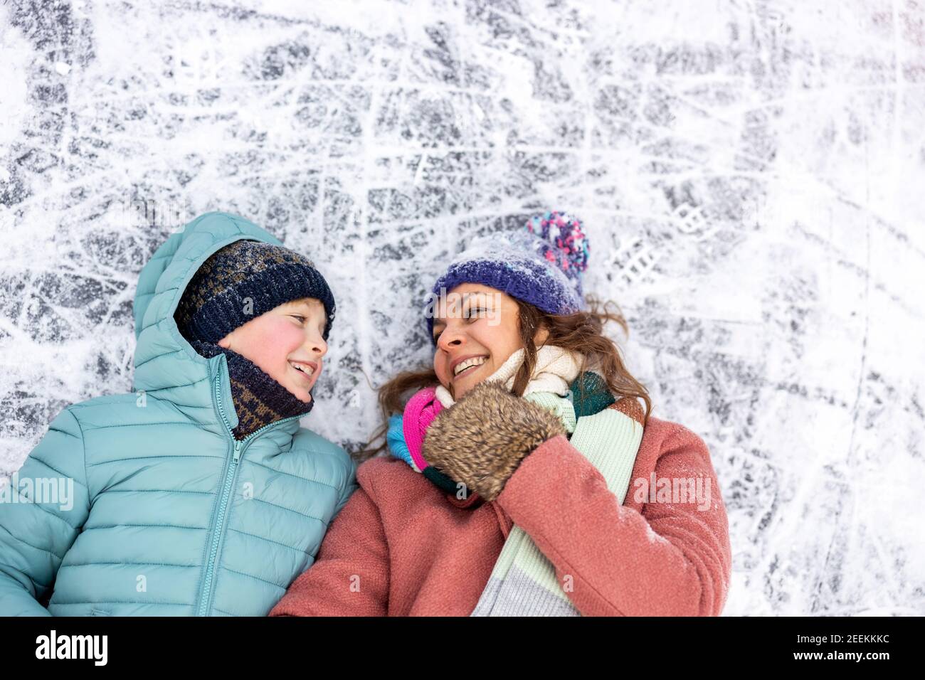 Madre e figlio sdraiati sulla superficie ghiacciata del lago e. sorridente Foto Stock