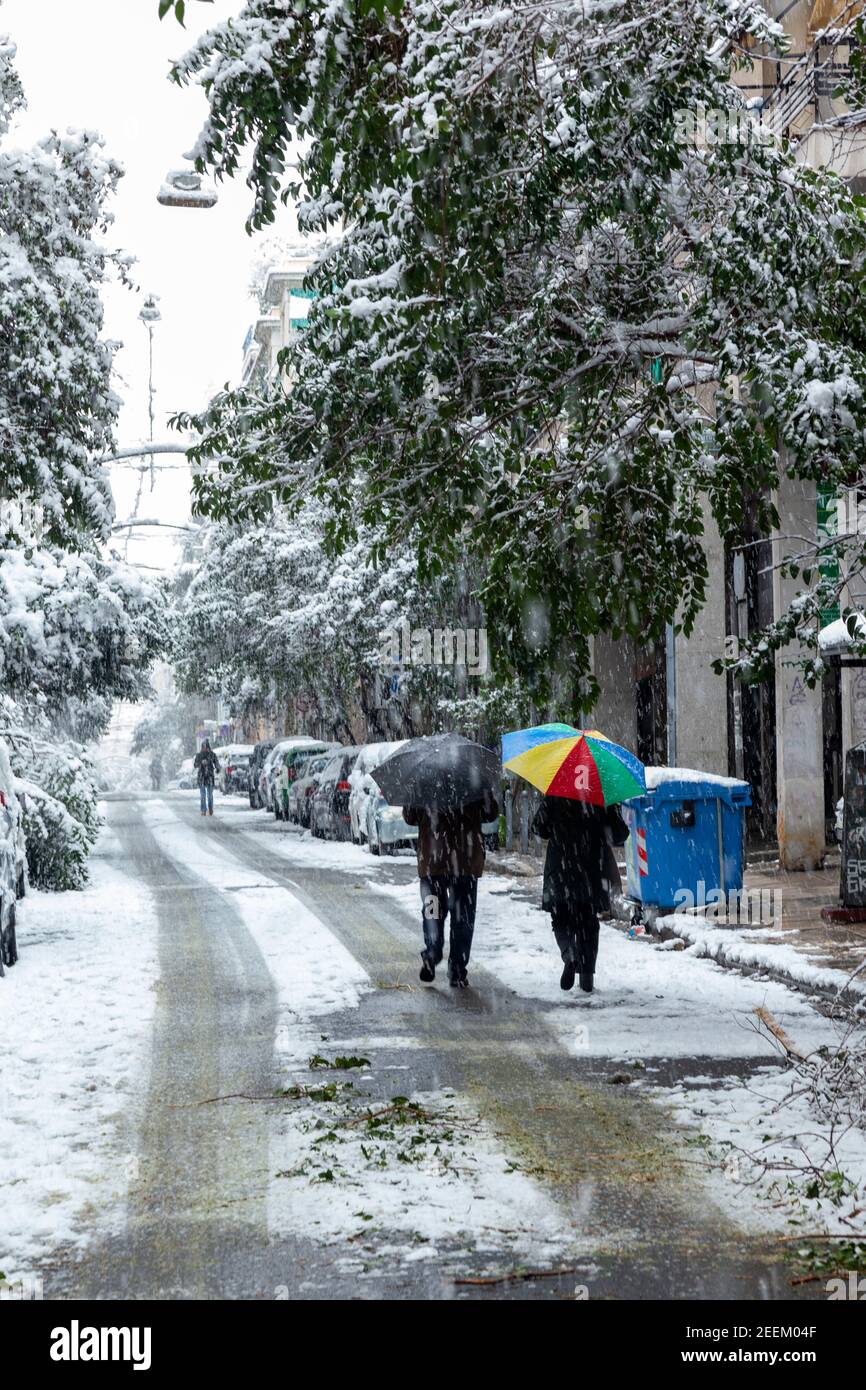 Una coppia cammina lungo la strada tenendo un ombrello colorato durante la tempesta di neve nella città di Atene, capitale della Grecia, Europa Foto Stock