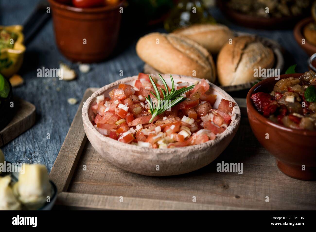 primo piano di un'insalata di pomodoro servita su una ciotola rustica su un tavolo rustico grigio accanto ad alcuni piatti e. ciotole con altri ingredienti vegetariani e contorno Foto Stock