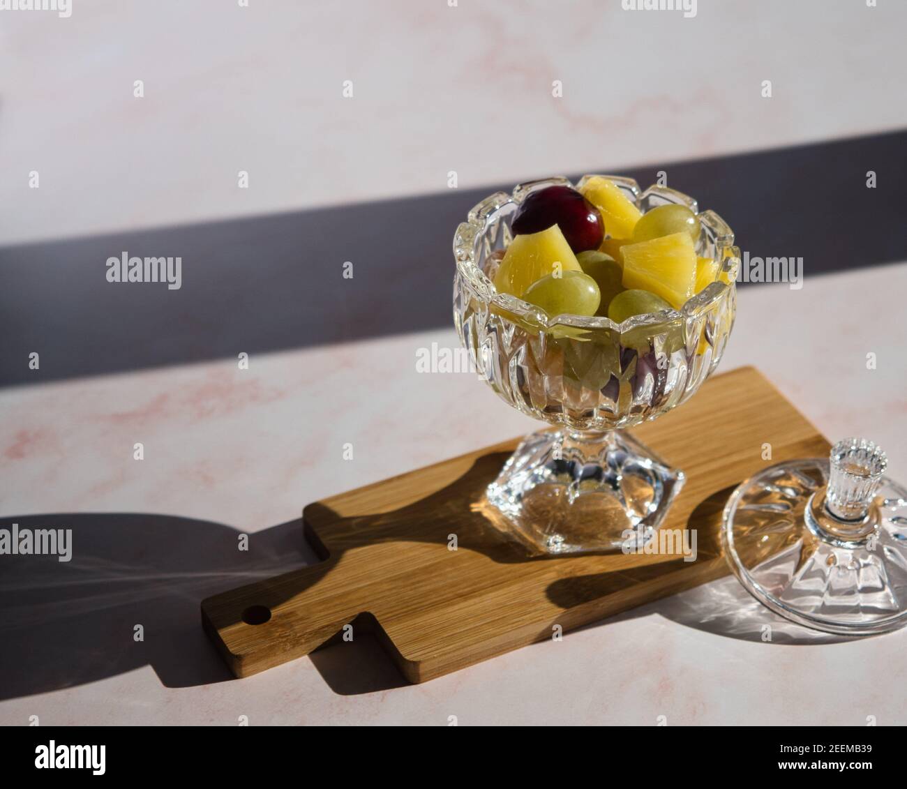 Gustosi pezzi di frutta in una tazza di vetro su tavola di legno e marmo rosa con luce estiva Foto Stock