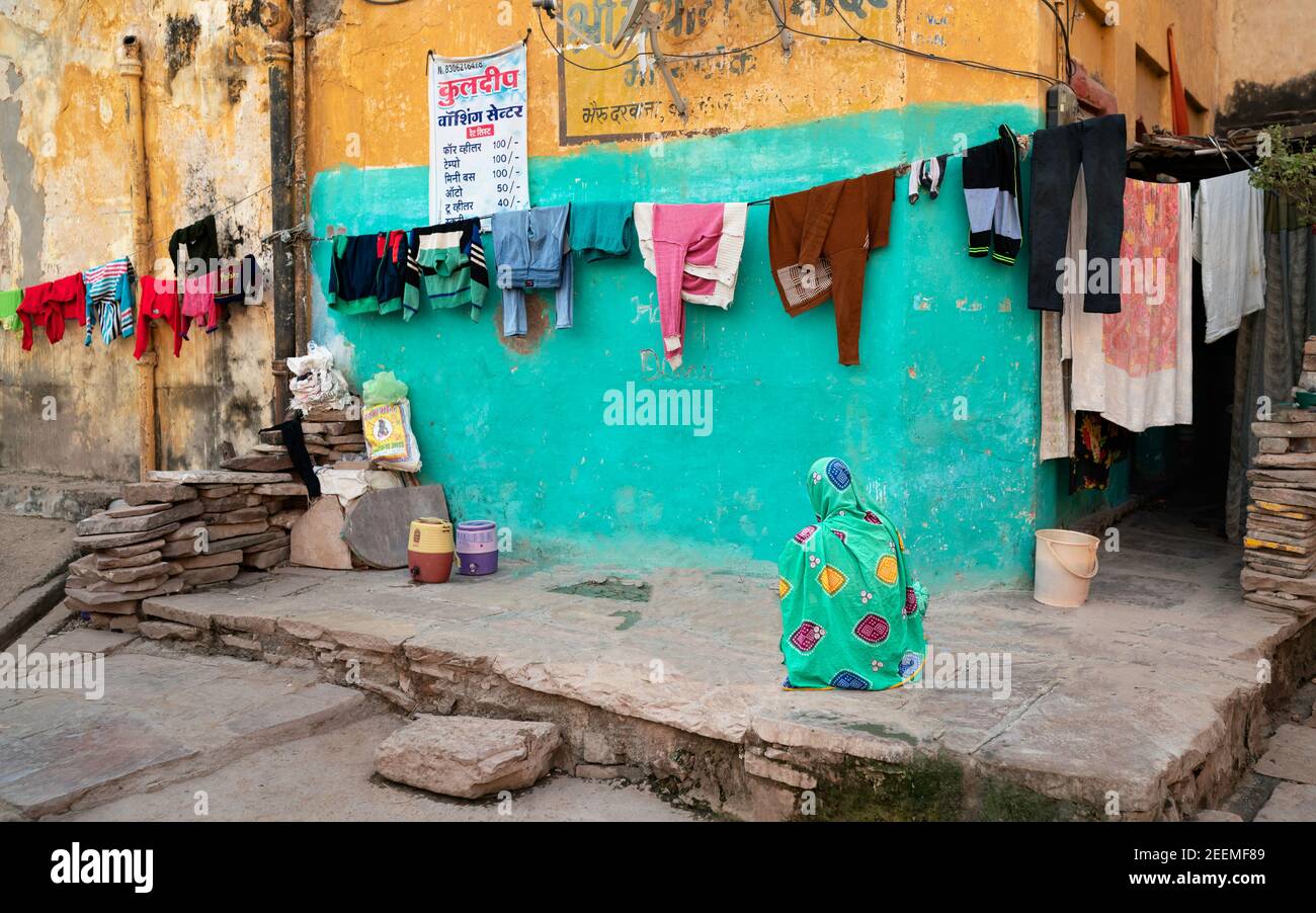 Donna, con piccola attività di lavanderia, seduta accanto a vestiti che asciugano fuori nella strada a Bundi, Rajasthan, India. Foto Stock