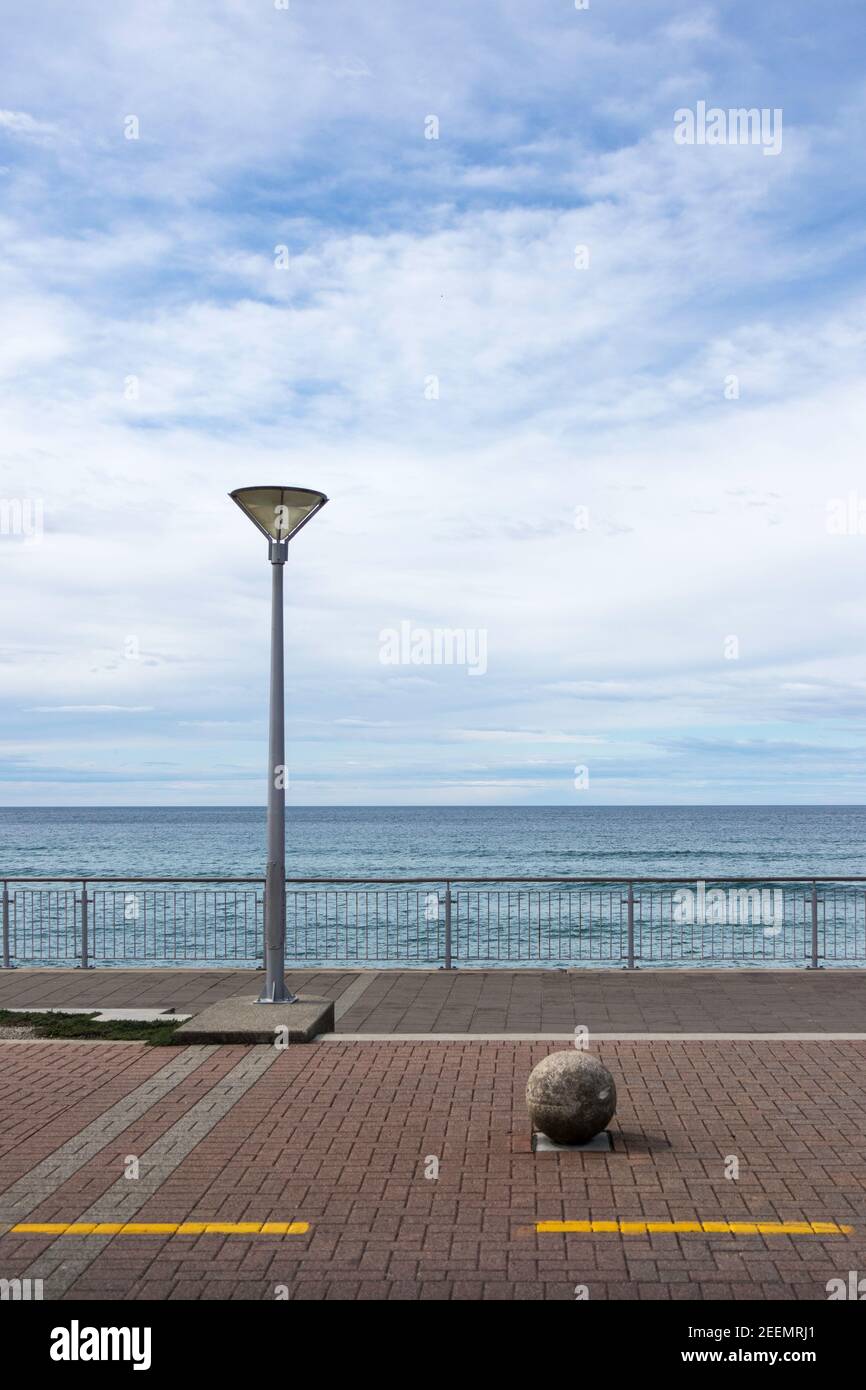 Esplanade a St Clair, Dunedin, Nuova Zelanda con un singolo lampione e un bollard sferico in cemento contro uno sfondo di mare e cielo blu, spazio copia Foto Stock