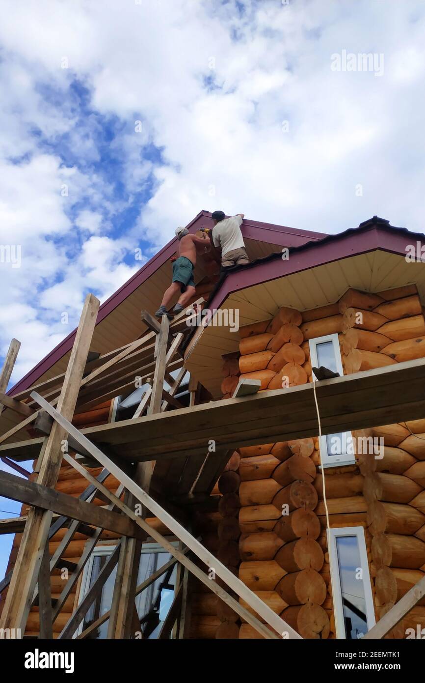 I lavoratori lavorano sulla parte superiore, isolamento del tetto e lavori di finitura sul tetto, ponteggi in legno.New Foto Stock