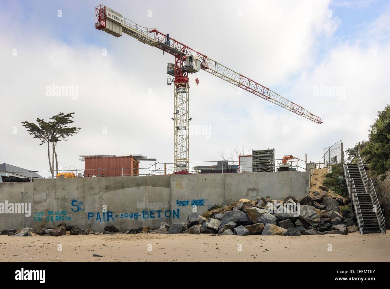 Cantiere con gru a torre, attrezzatura, lone alla spiaggia di St Pair-sur-Mer, Normandia, con graffiti sarcastici che protestano l'edificio Foto Stock