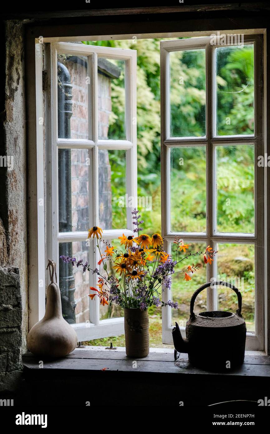Mostra di fiori da una finestra aperta in un cottage inglese tradizionale. Foto Stock