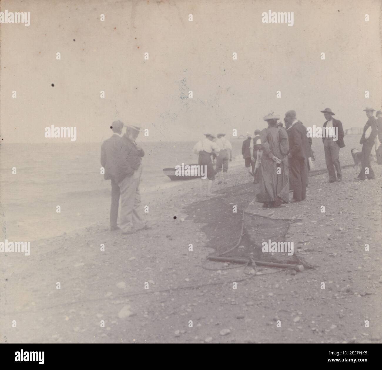 Fotografia edoardiana d'epoca del 1904 che mostra un gruppo di persone sulla spiaggia con i pescatori e le loro reti da pesca. Foto Stock