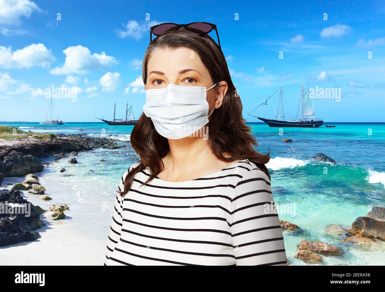 Viaggio verso una destinazione soleggiata durante la corona o covid pandemic: turistico con occhiali da sole e maschera medica viso di fronte a una spiaggia tropicale. Foto Stock