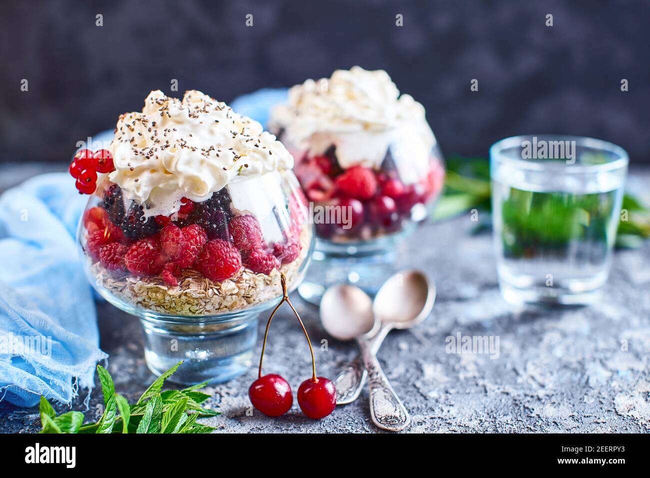 Idee di ricetta per la colazione di dieta estiva, dessert sano del mattino in vasi porzionati con frutti di bosco estivi - lampone, ciliegie, mora. Su fondo di pietra. Foto Stock