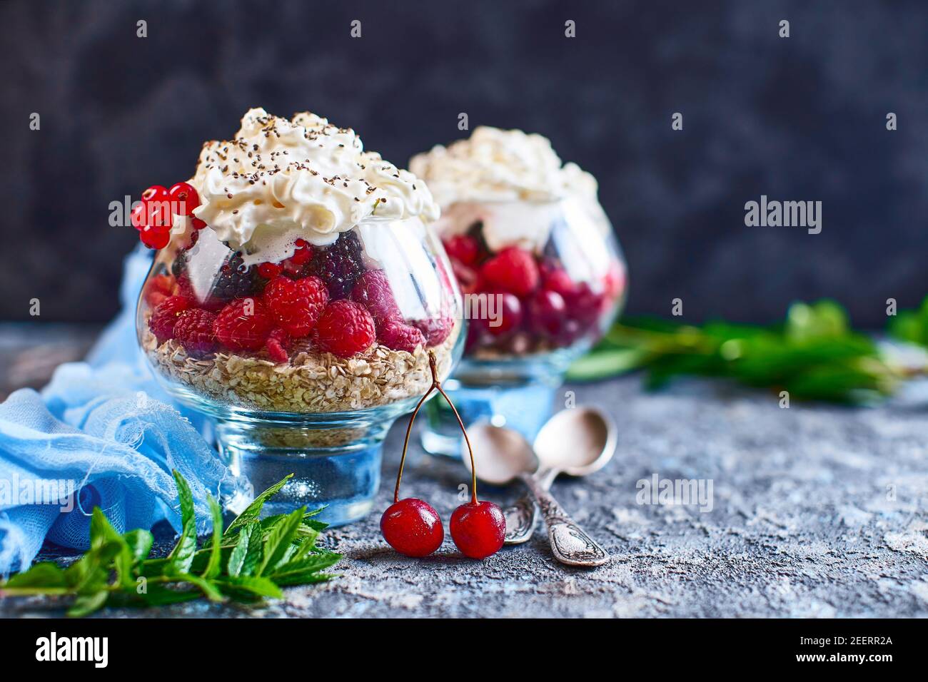 Idee di ricetta per la colazione di dieta estiva, dessert sano del mattino in vasi porzionati con frutti di bosco estivi - lampone, ciliegie, mora. Su fondo di pietra. Foto Stock