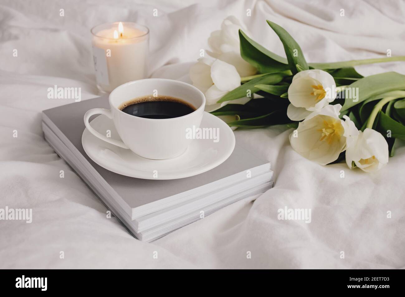 Caffè, candela e tulipani bianchi a letto. Foto Stock
