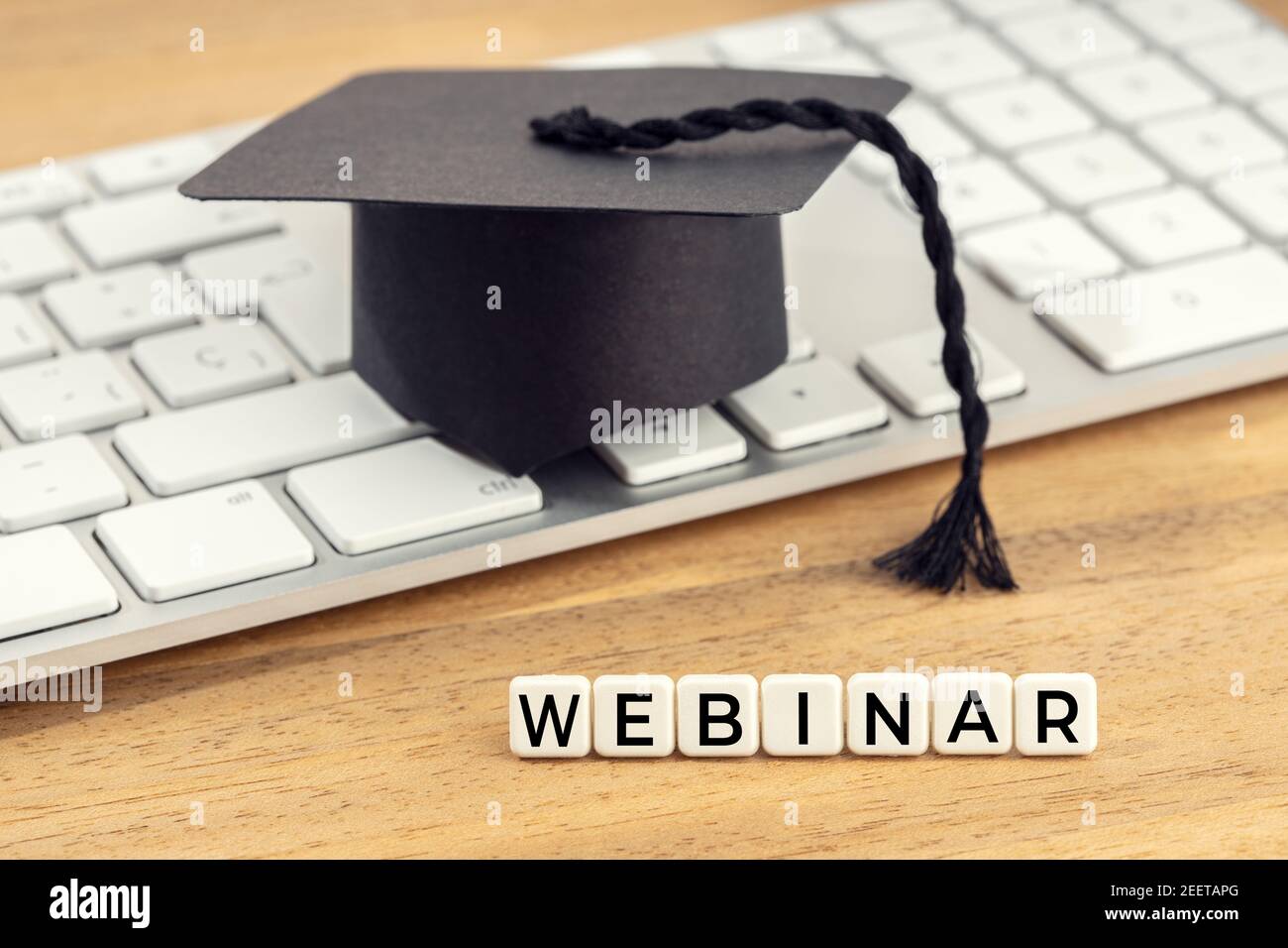 Concetto di webinar. Berretto graduato sulla tastiera del computer sulla scrivania in legno Foto Stock