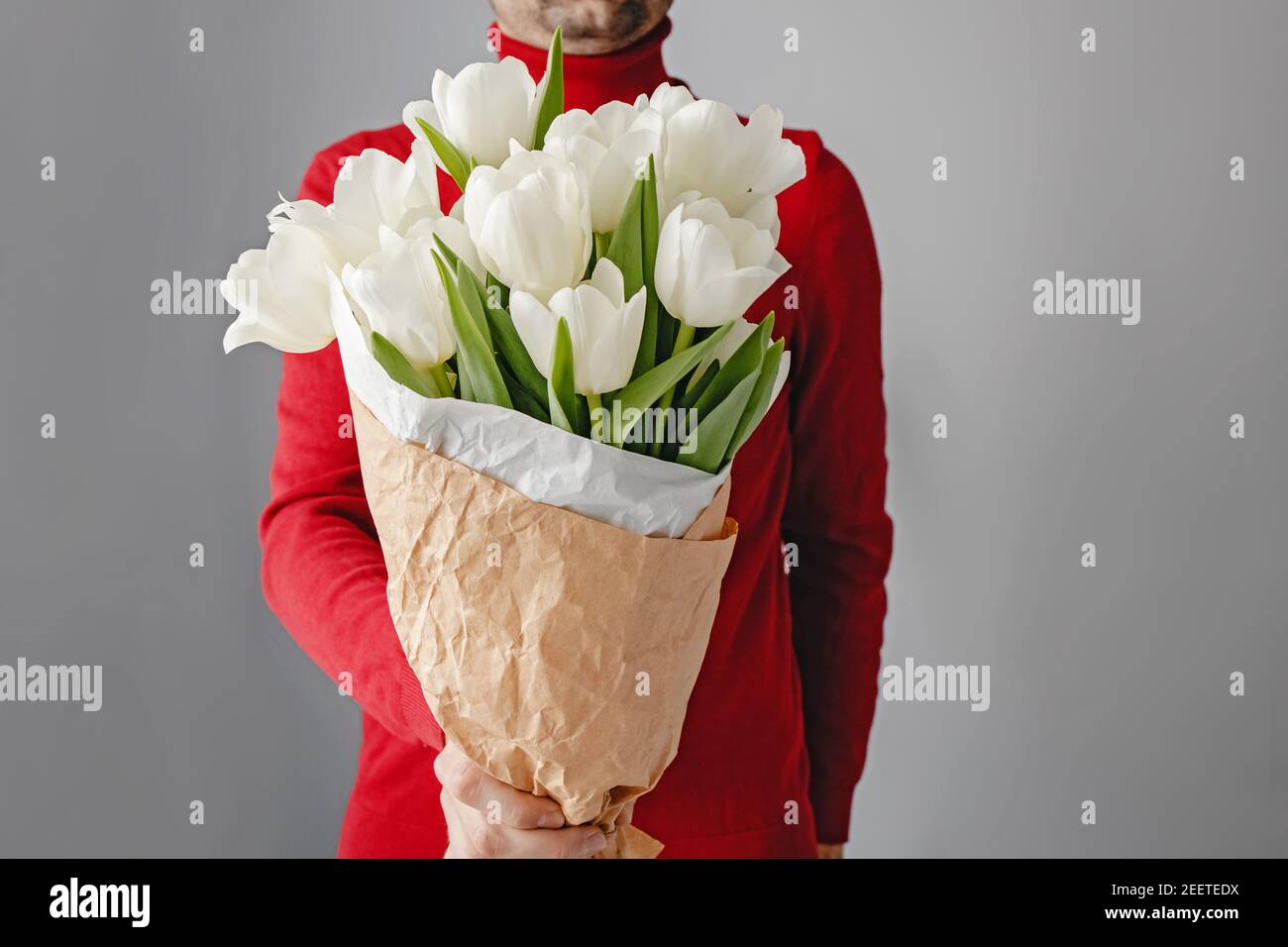 Uomo in pullover rosso con bouquet di tulis bianco. Foto Stock