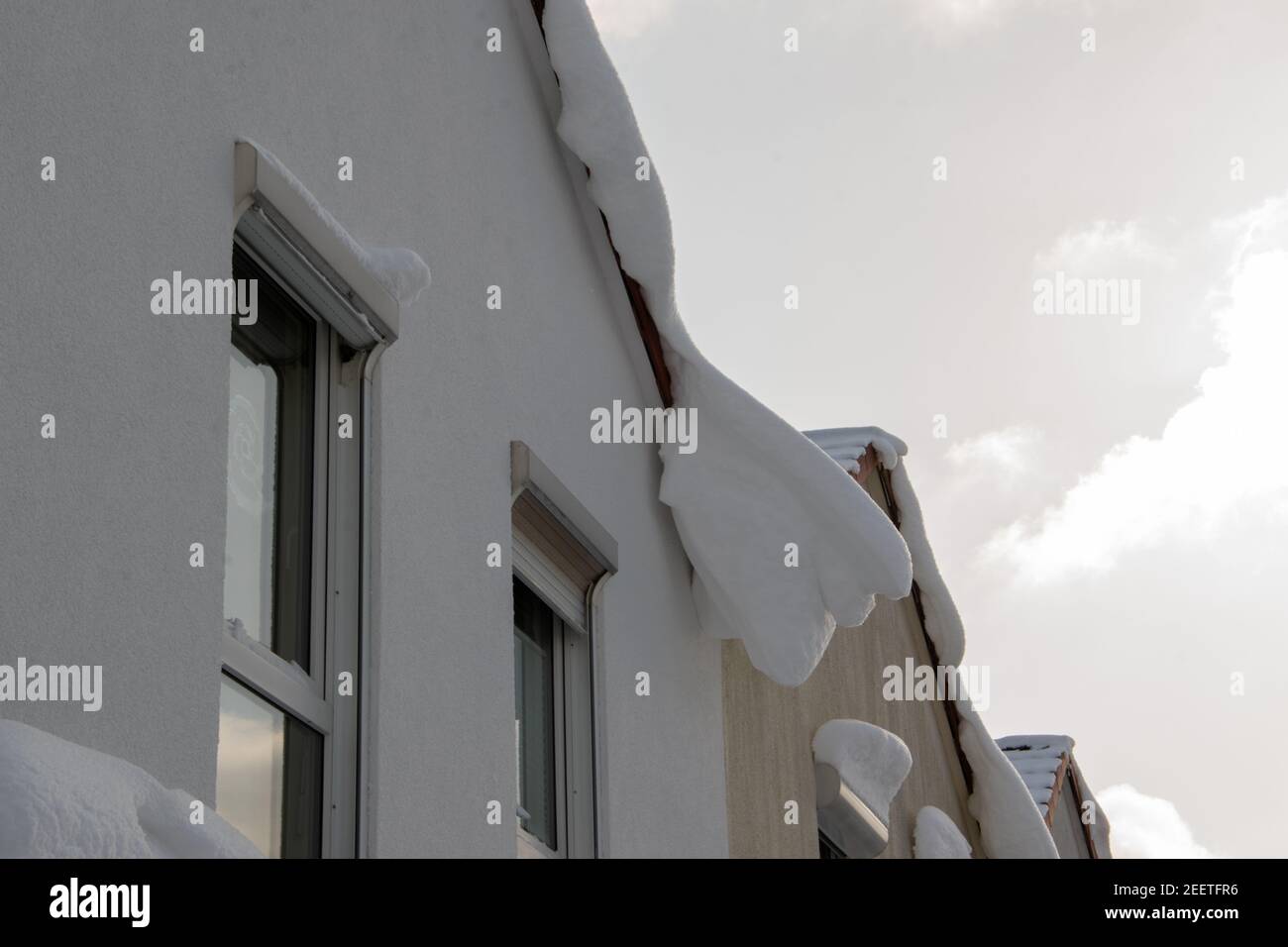Un sacco di neve su un tetto di una fila di case. Sta già appendere lontano e sta per schiantarsi. Foto Stock