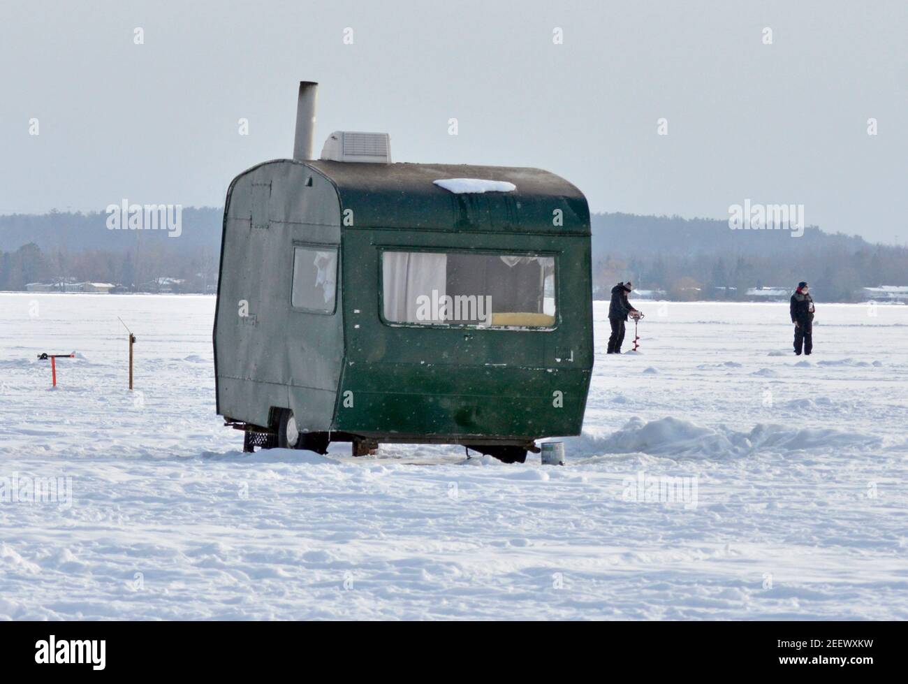 Due persone hanno creato un nuovo buco per la pesca sul ghiaccio dietro una baraccopoli Foto Stock