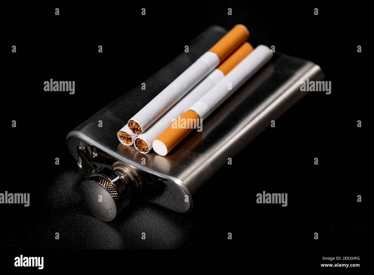 Matracci di metallo e sigarette. Contenitore metallico per alcool e tabacco da fumo. Sfondo scuro. Foto Stock