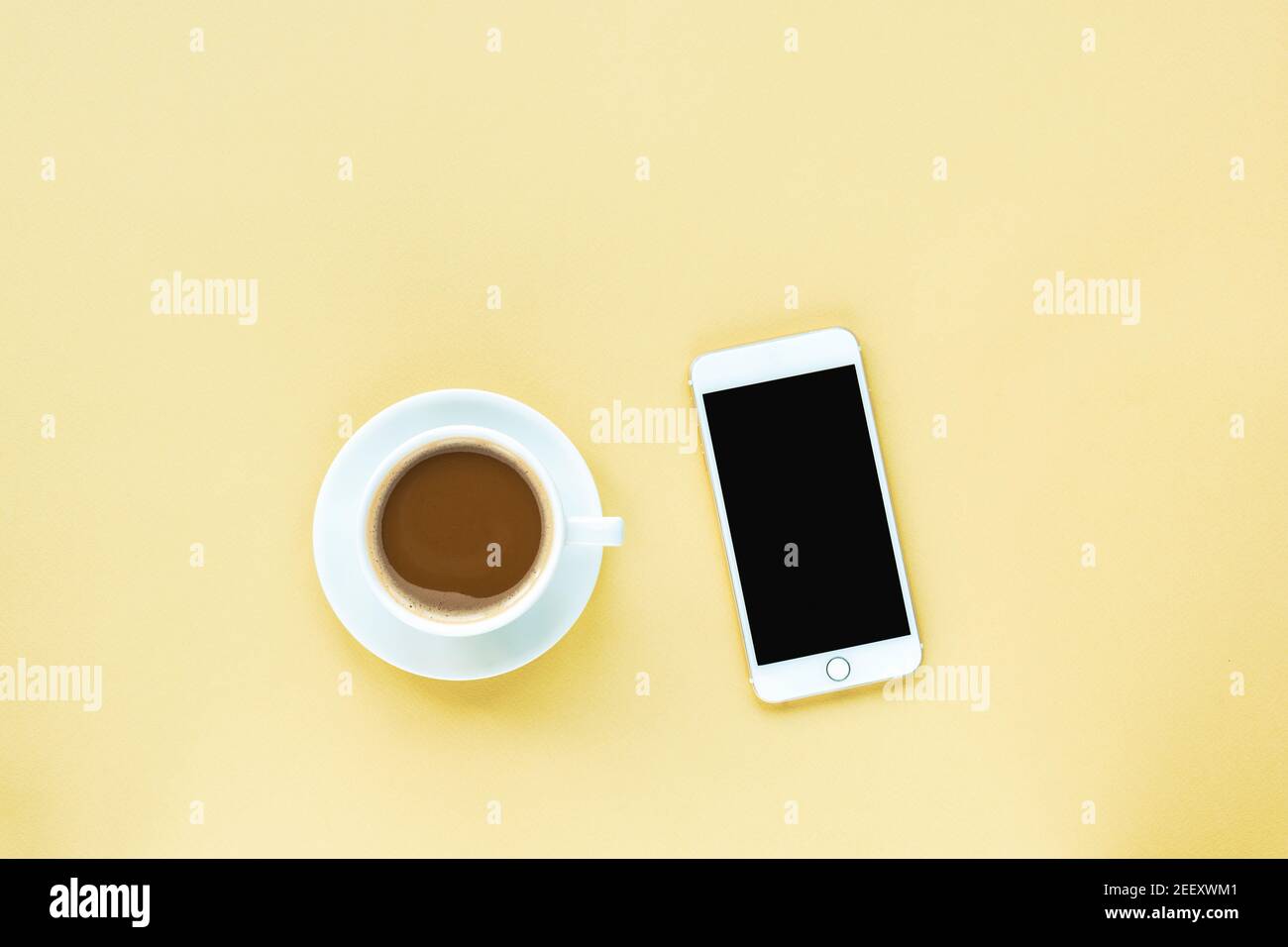 Tazza di caffè e cellulare su sfondo giallo. Vista dall'alto, disposizione piatta. Foto Stock