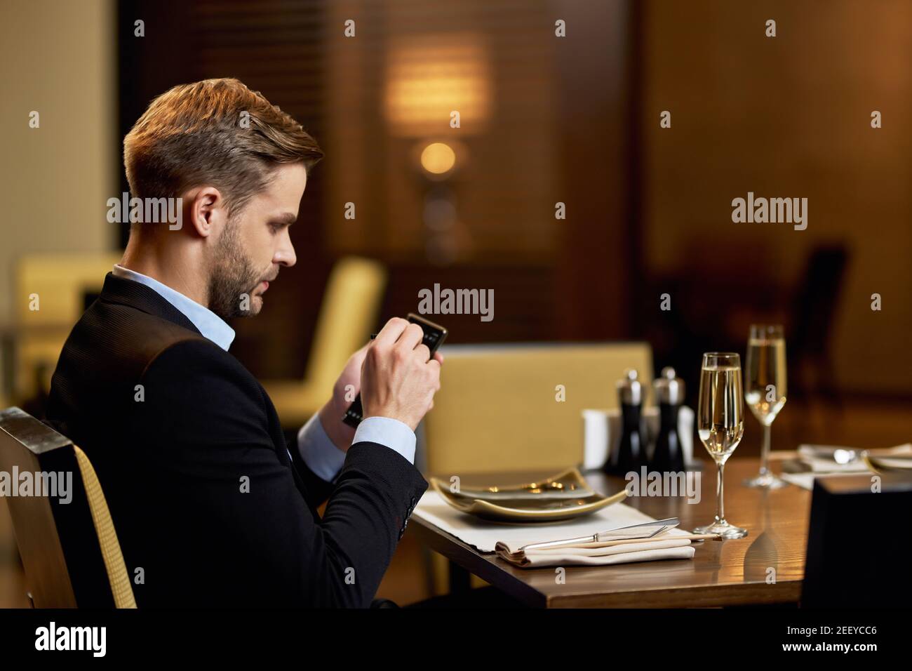 Copia la foto spaziale di un seripo uomo dai capelli giusti in tuta guardando con attenzione il suo smartphone mentre si siede al tavolo del ristorante Foto Stock