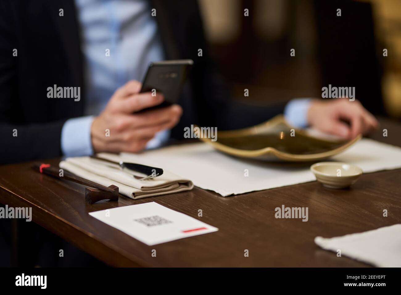 Foto sfocata ritagliata dell'uomo in tuta che tiene lo smartphone mentre seduto al tavolo del ristorante Foto Stock