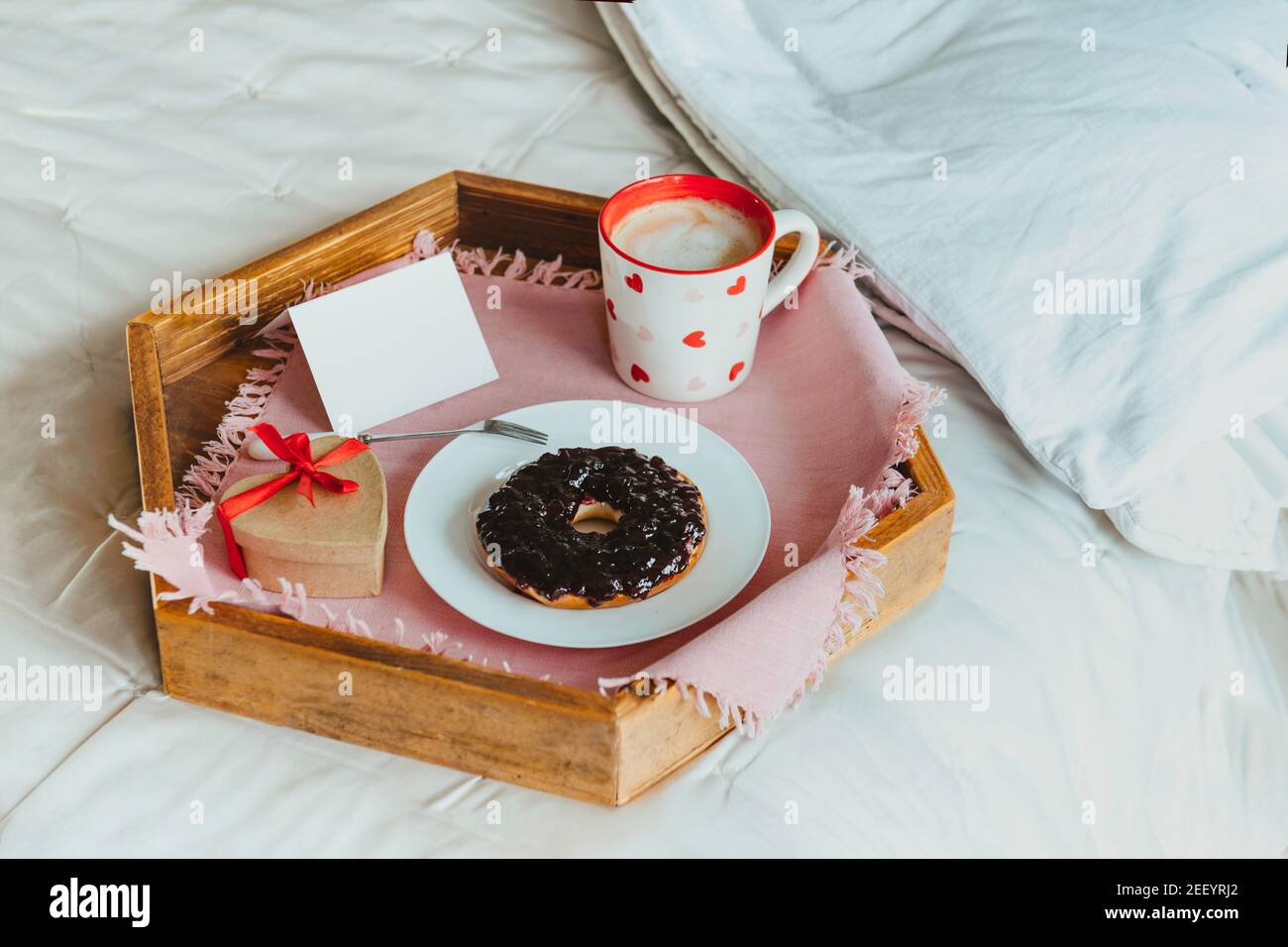 Semplice colazione di San Valentino a letto per l'amante. Una tazza di caffè e bagel con marmellata, scatola regalo a forma di cuore con nastro rosso, carta vuota vuota per Foto Stock
