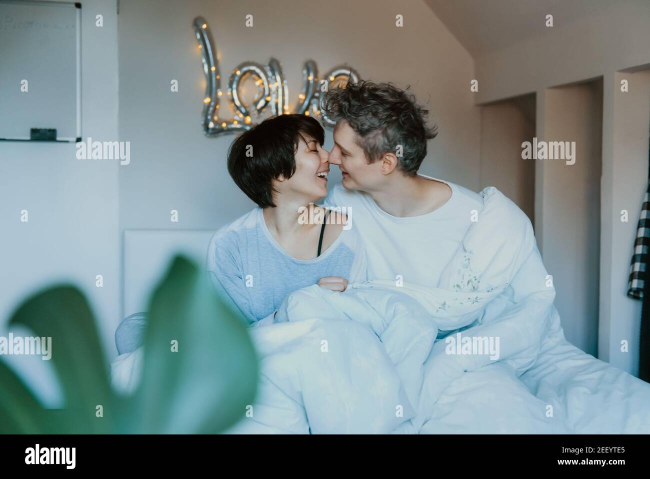 Coppia amorevole in pigiama divertirsi a letto nella camera da letto con la parola Amore sullo sfondo della parete. Stanno abbracciando e ridendo. Buona famiglia Foto Stock