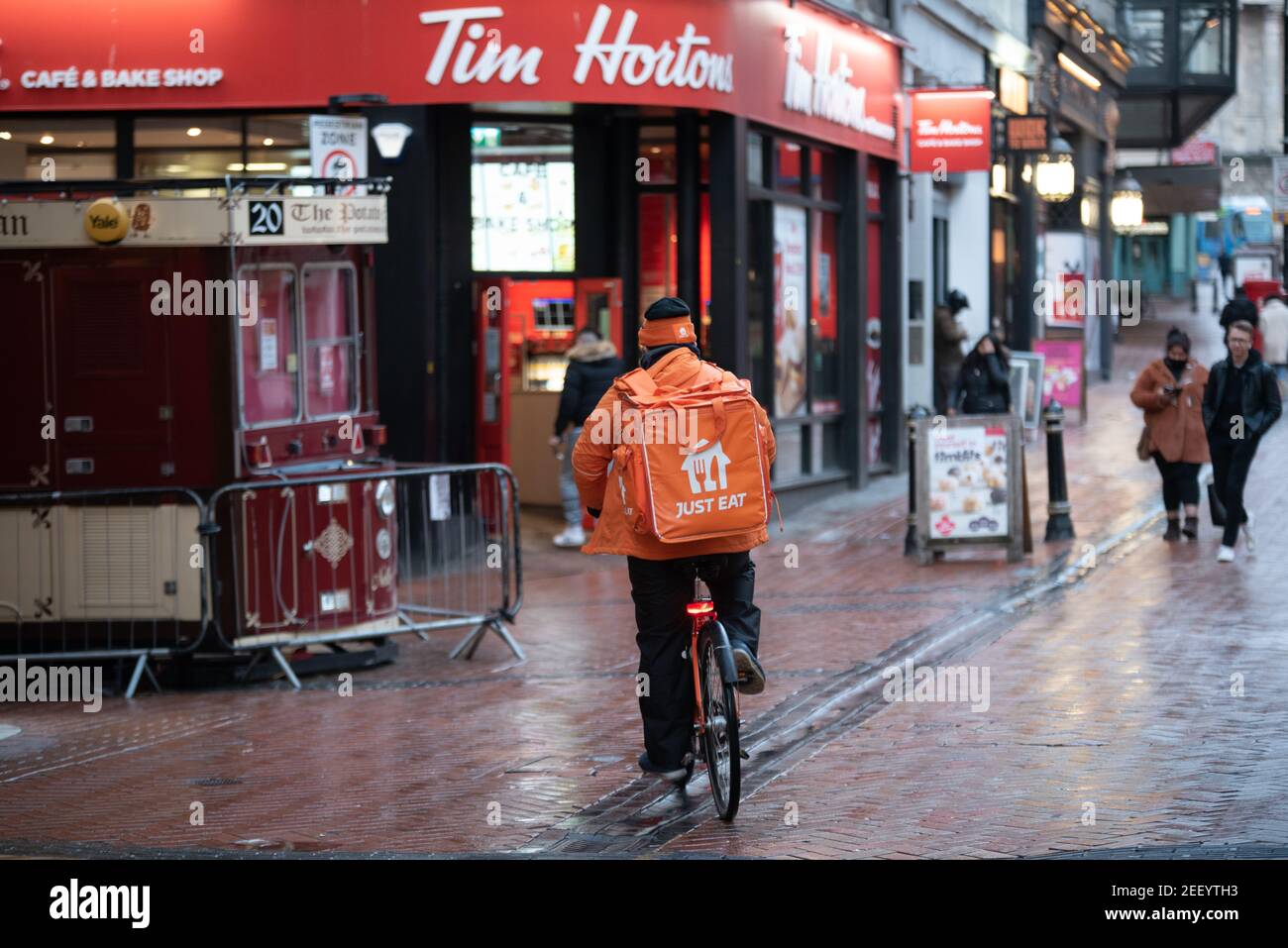 Mangia solo il pilota con consegna in abito arancione con una moto di marca Just Eat, passando dal Tim Hortons cafe a Birmingham New Street, West Midlands, Regno Unito Foto Stock