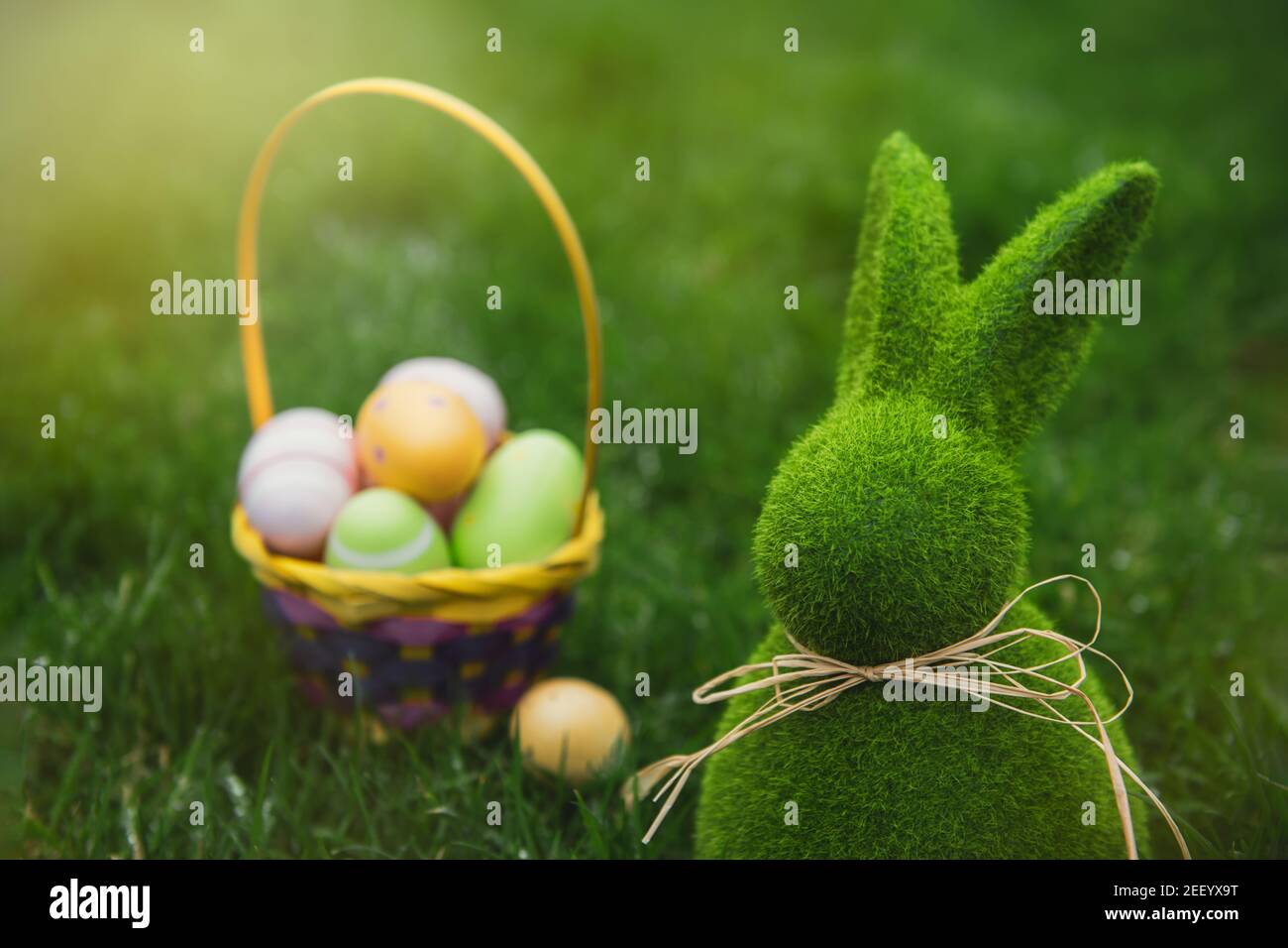 Primo piano coniglietto di Pasqua statuetta di coniglio e cesto con uova di pasqua sul prato verde erba sfondo. Caccia all'uovo di Pasqua in giardino. Messa a fuoco selettiva Foto Stock