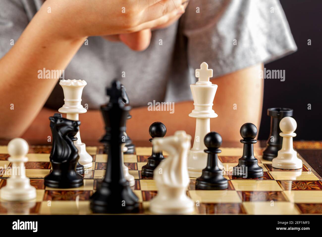 Un ragazzo caucasico è in pensieri profondi con la mano sulla fronte durante una partita a scacchi. Sta guardando giù con una posizione preoccupata. Immagine versatile Foto Stock