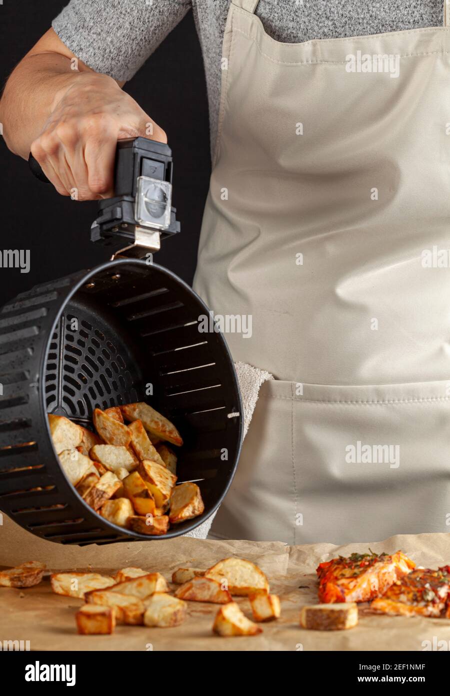 Una donna caucasica cuoca sta scaricando la patata fritta appena fatta trita su un pezzo di carta da forno che ha tre filetto di salmone marinato arrosto al forno con Foto Stock