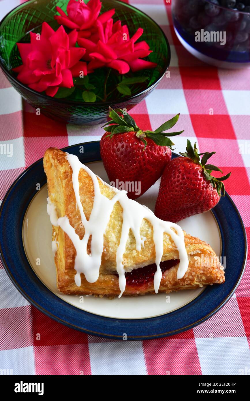 Frosted Strawberry Croissant intonacato con frutta fresca su Rosso e. Tovaglia bianca Foto Stock