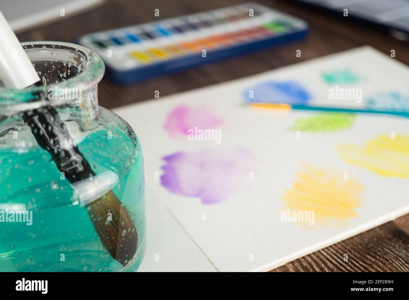 Vernici ad acqua e tamponi di disegno disposti sul piano del tavolo. Colori vivaci e forme astratte di doodle con pennello in acqua verde a fuoco in foregroun Foto Stock