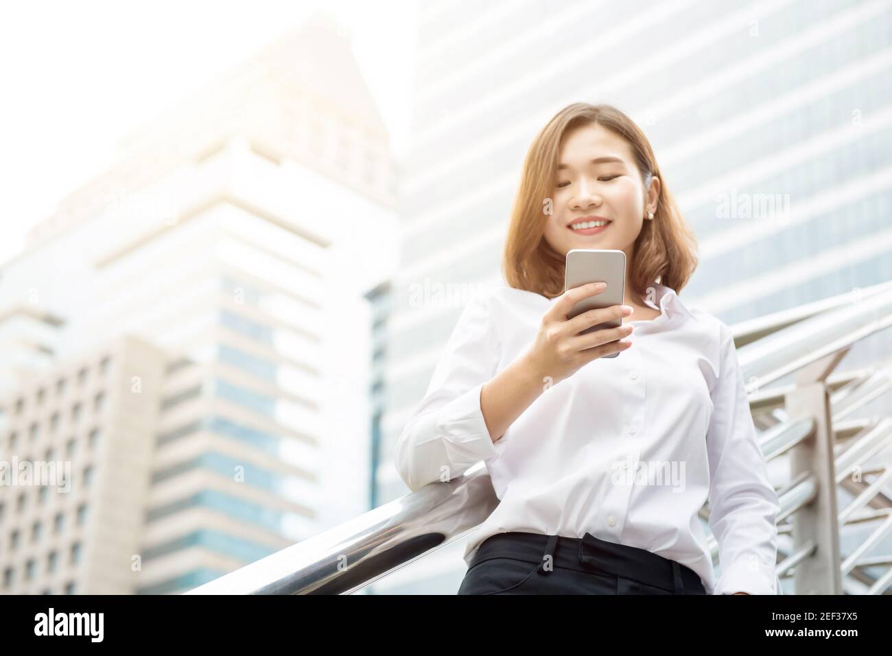 Donna d'affari asiatica che usa lo smartphone all'aperto sullo sfondo offuscato dell'edificio dell'ufficio in città Foto Stock