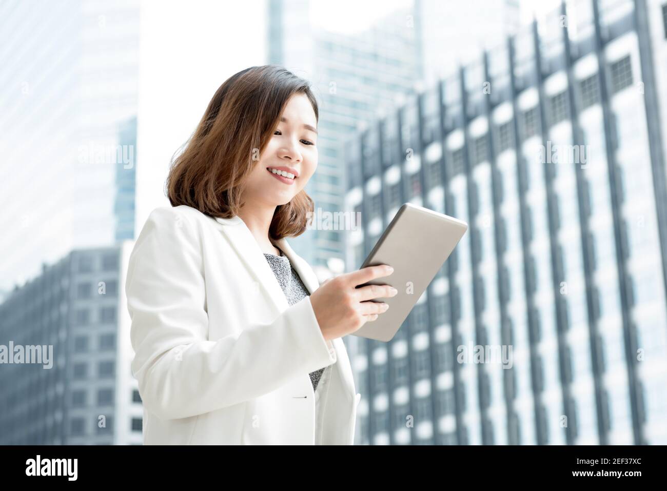 Donna d'affari asiatica che usa il computer tablet all'aperto nell'edificio offuscato dell'ufficio sfondo della città Foto Stock